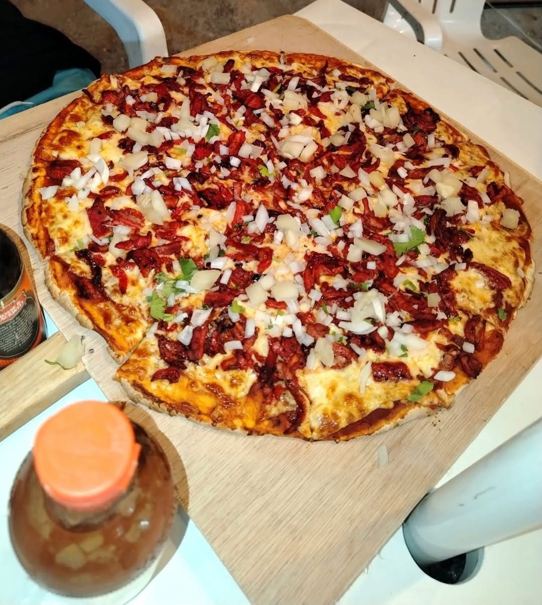Pizza casera en bandeja de madera con abundante tomate, jamón, cebolla y queso gratinado.