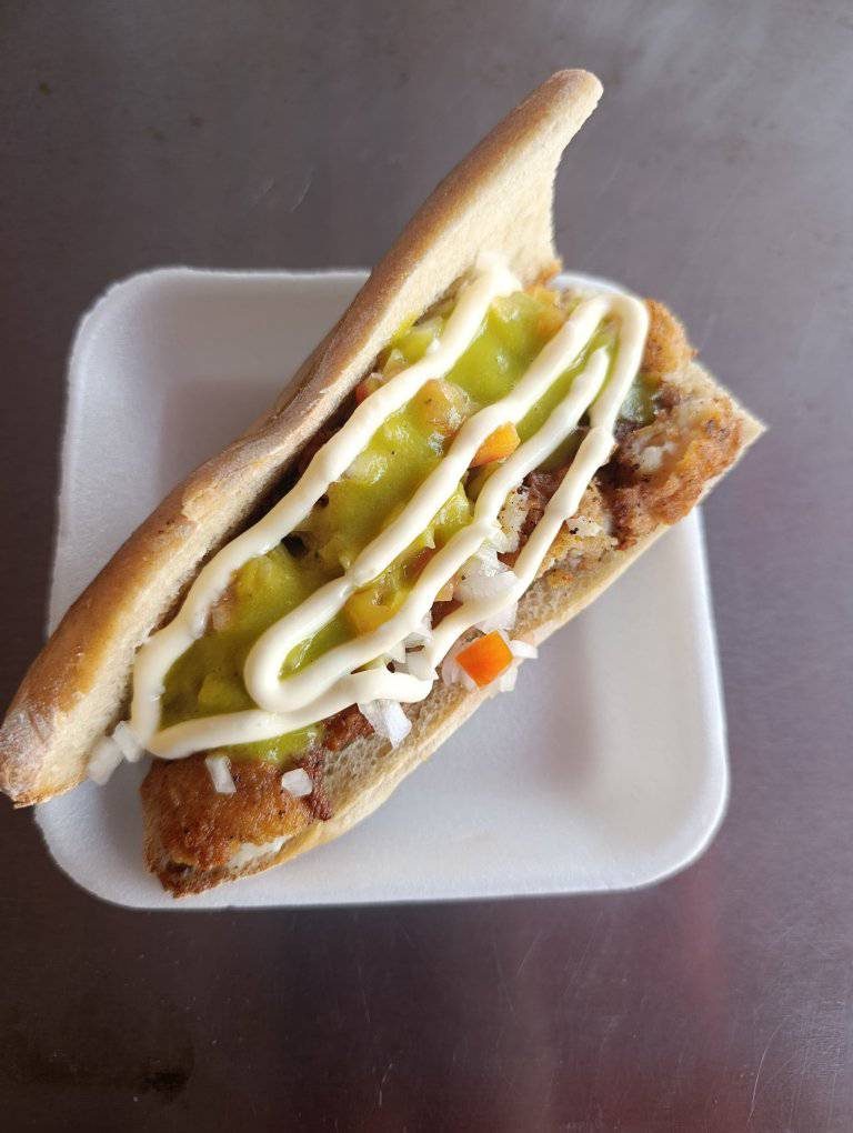 Sándwich gourmet con pan tostado, mayonesa, carne y vegetales en plato blanco.